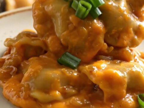 A close-up of a ceramic crockpot filled with cheesy pierogies and kielbasa, garnished with green onions.
