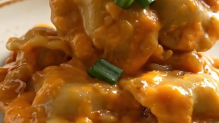 A close-up of a ceramic crockpot filled with cheesy pierogies and kielbasa, garnished with green onions.