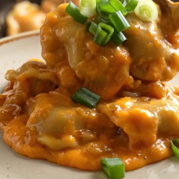 A close-up of a ceramic crockpot filled with cheesy pierogies and kielbasa, garnished with green onions.