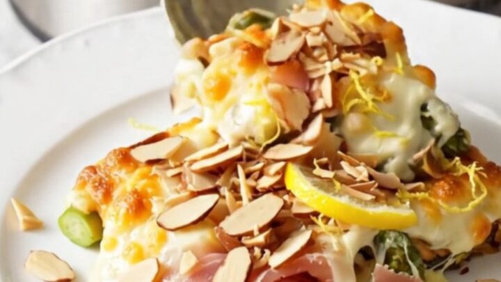 A close-up of cheesy asparagus and prosciutto gratin in a stainless steel slow cooker, bubbling with melted cheese.