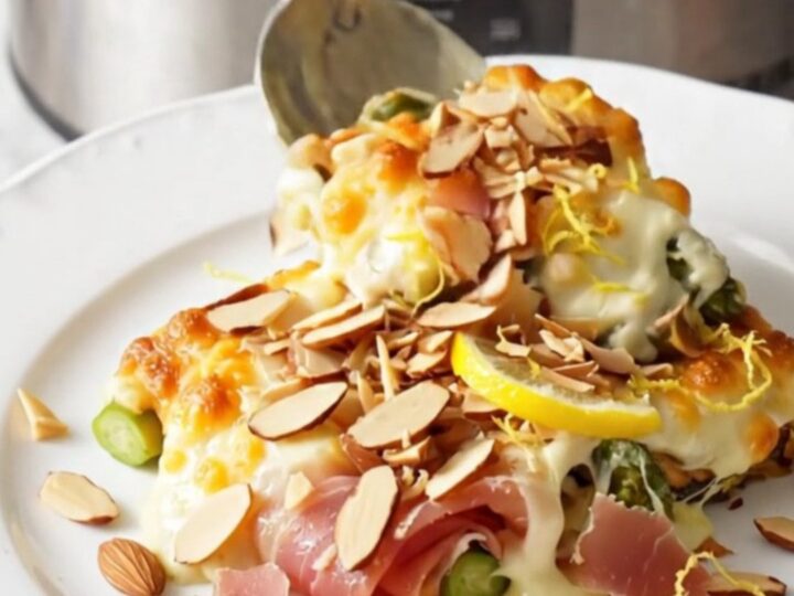 A close-up of cheesy asparagus and prosciutto gratin in a stainless steel slow cooker, bubbling with melted cheese.