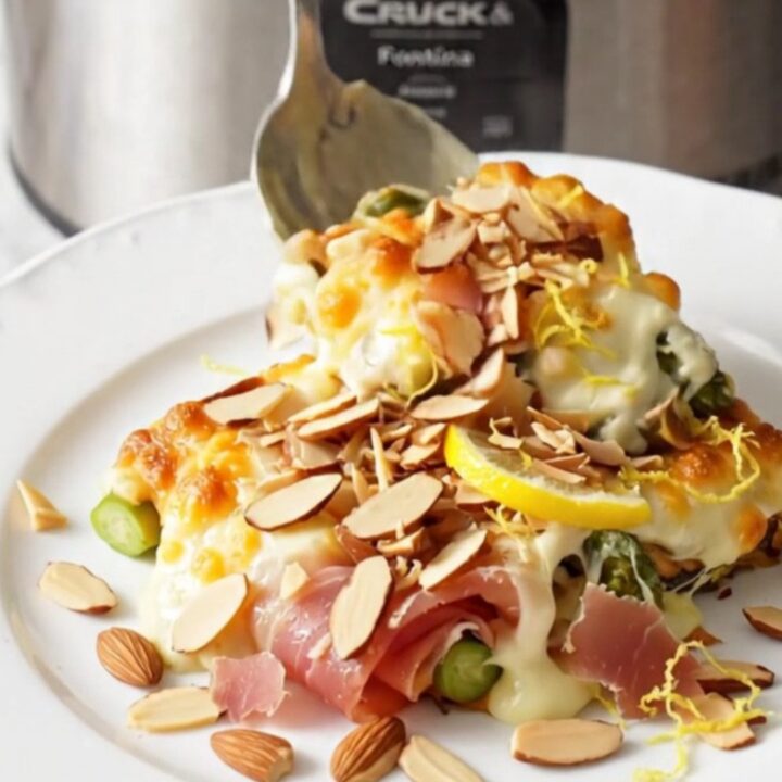 A close-up of cheesy asparagus and prosciutto gratin in a stainless steel slow cooker, bubbling with melted cheese.