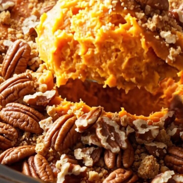 A warm, steaming portion of sweet potato casserole topped with a golden, crunchy pecan praline crust in a ceramic bowl.