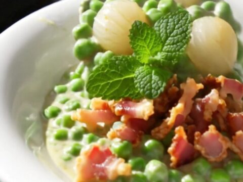 A close-up view of creamy peas and pearl onions in a mint-green slow cooker, garnished with crispy pancetta.