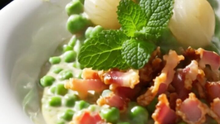 A close-up view of creamy peas and pearl onions in a mint-green slow cooker, garnished with crispy pancetta.