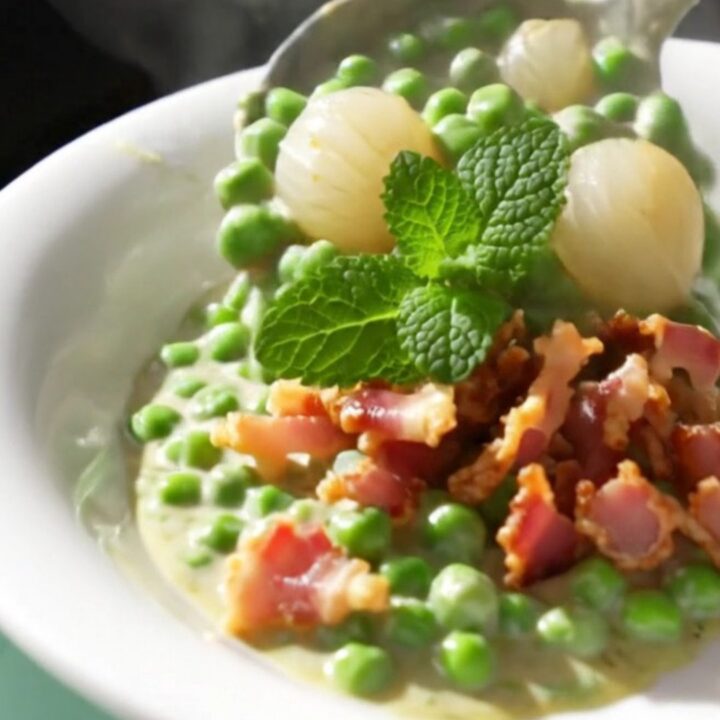 A close-up view of creamy peas and pearl onions in a mint-green slow cooker, garnished with crispy pancetta.