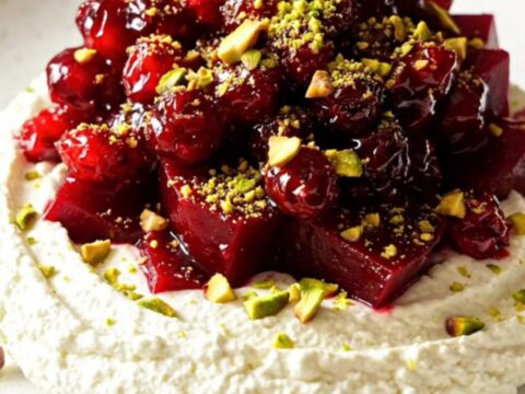 Slow-cooker cranberry orange glazed beets arranged over whipped chevre cheese with pistachios on a platter.