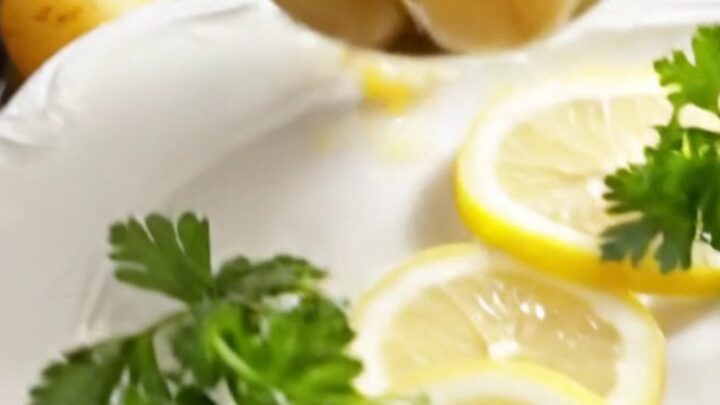 A white ceramic slow cooker filled with golden baby potatoes and artichoke hearts in a lemon butter sauce.