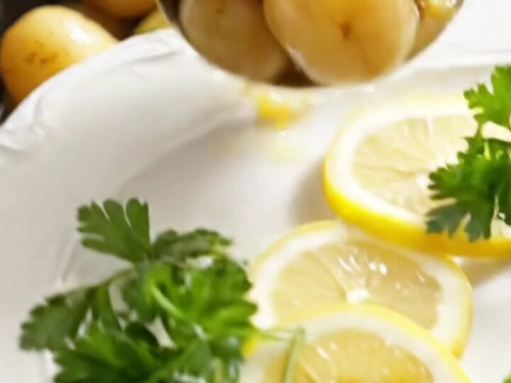 A white ceramic slow cooker filled with golden baby potatoes and artichoke hearts in a lemon butter sauce.
