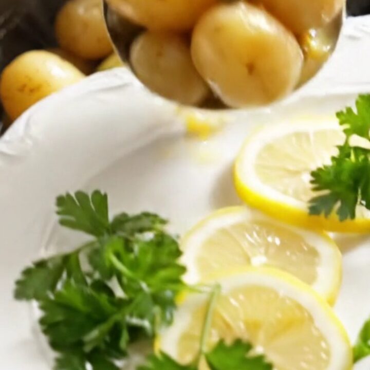 A white ceramic slow cooker filled with golden baby potatoes and artichoke hearts in a lemon butter sauce.