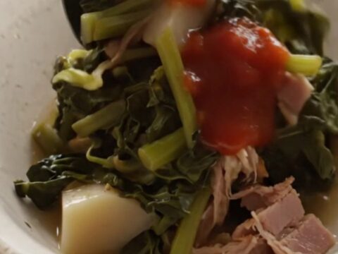 A close-up of a bowl filled with steaming turnip greens, diced turnip roots, and shredded ham in a savory broth.
