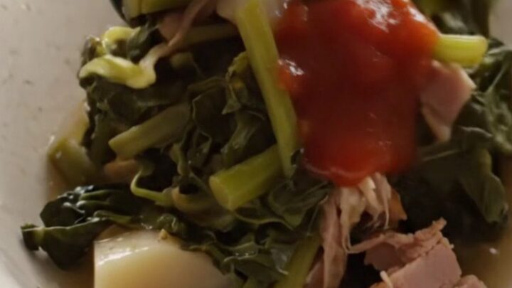 A close-up of a bowl filled with steaming turnip greens, diced turnip roots, and shredded ham in a savory broth.