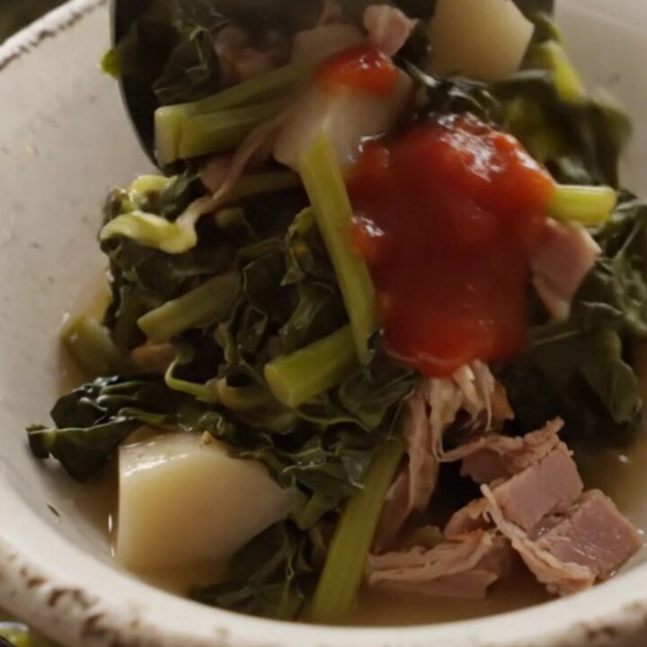 A close-up of a bowl filled with steaming turnip greens, diced turnip roots, and shredded ham in a savory broth.