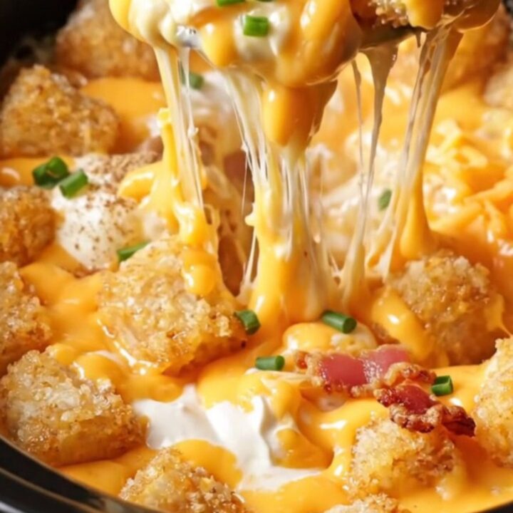 A steaming, cheesy bacon ranch tater tot casserole in a slow cooker, topped with chopped chives.