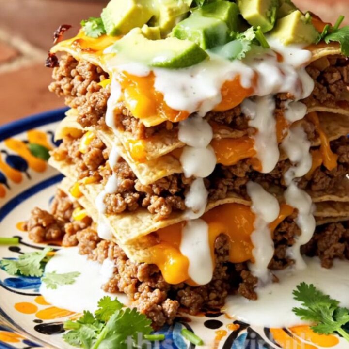 A tall, steaming wedge of stacked beef and red chile enchilada casserole on a colorful Talavera plate.