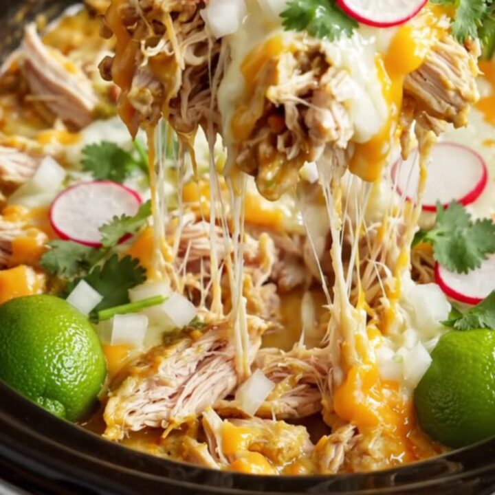A steaming casserole dish filled with triple-cheese Suiza chicken enchiladas in a rustic
