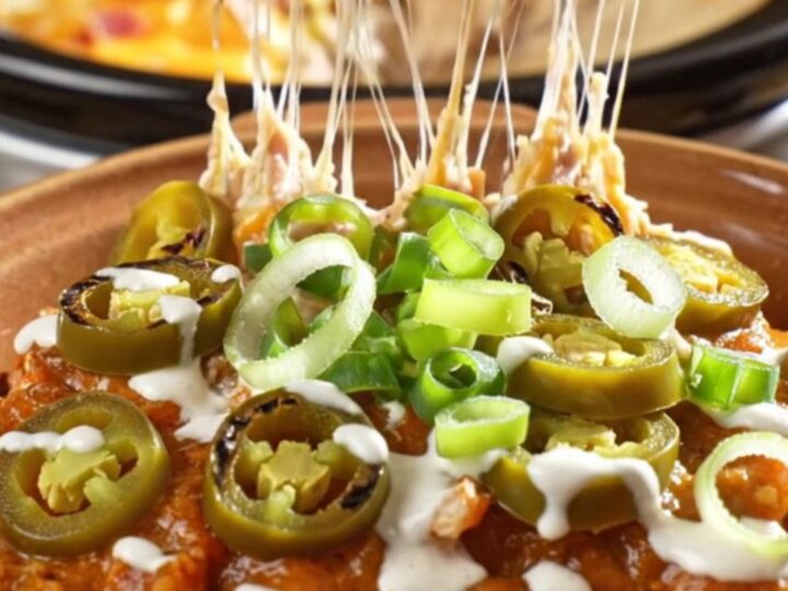 A creamy, cheesy chicken enchilada casserole in a slow cooker with visible bacon and jalapeño garnishes.
