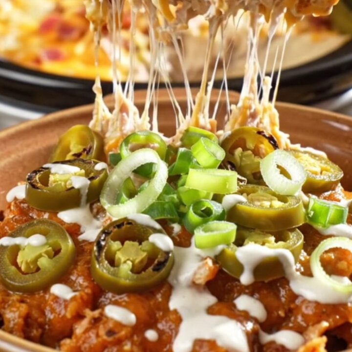 A creamy, cheesy chicken enchilada casserole in a slow cooker with visible bacon and jalapeño garnishes.
