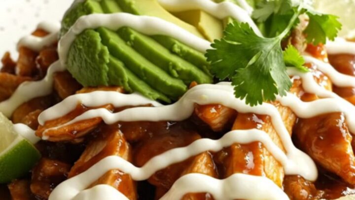 A close-up of slow-cooked chicken fajitas with mango, peppers, and melted cheese in a glossy orange pot.