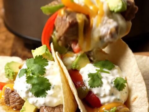 A rustic slow cooker filled with tender steak bites, colorful peppers, and melted pepper jack cheese.