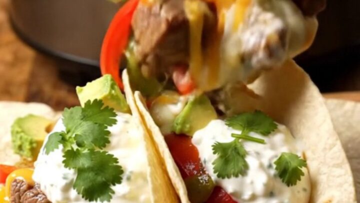 A rustic slow cooker filled with tender steak bites, colorful peppers, and melted pepper jack cheese.