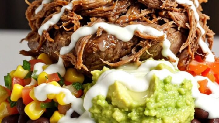 A close-up of a slow-cooker filled with shredded beef barbacoa in a rich, dark red adobo sauce.