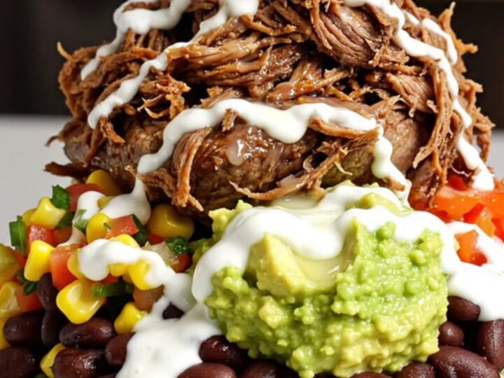A close-up of a slow-cooker filled with shredded beef barbacoa in a rich, dark red adobo sauce.