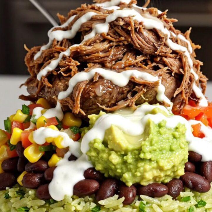 A close-up of a slow-cooker filled with shredded beef barbacoa in a rich, dark red adobo sauce.