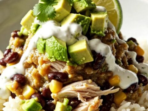 A steaming bowl of cilantro lime chicken burrito bowls topped with melted cheese, avocado, and sour cream.