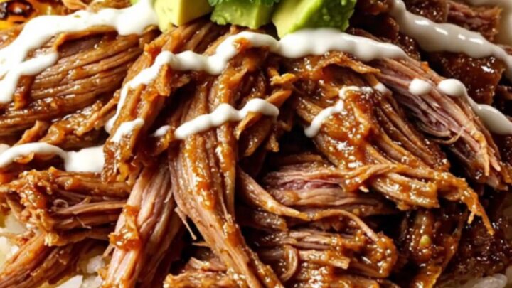A top-down view of a burrito bowl featuring shredded beef, melted cheese, charred corn, and avocado.