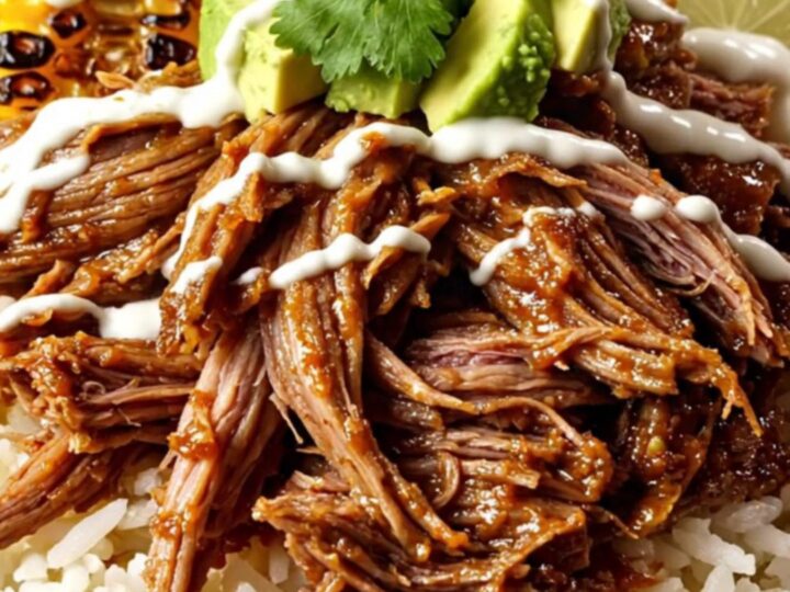 A top-down view of a burrito bowl featuring shredded beef, melted cheese, charred corn, and avocado.