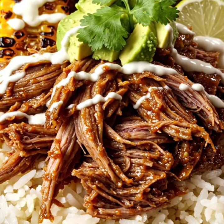 A top-down view of a burrito bowl featuring shredded beef, melted cheese, charred corn, and avocado.