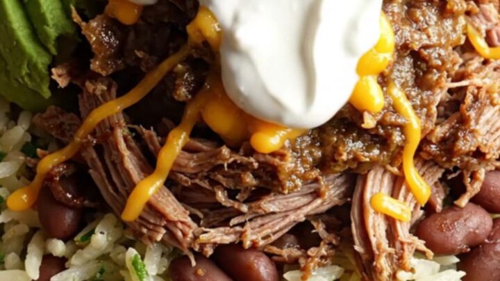 A close-up of a slow cooker filled with shredded beef brisket and melted cheese, with steam rising.