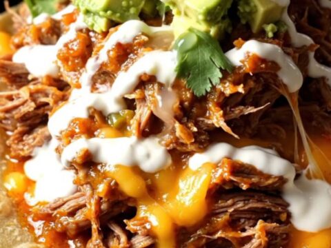 A stainless steel crockpot filled with shredded beef in a red chile sauce topped with melted Oaxaca cheese.