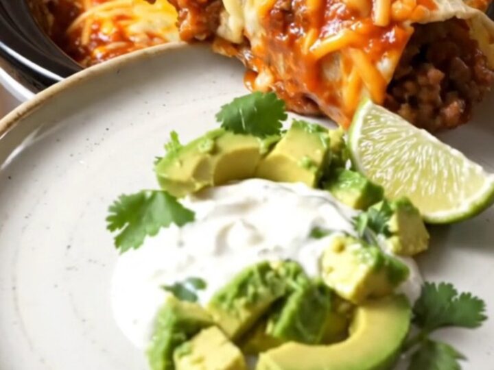 A row of beef and bean burritos in a slow cooker, smothered in red and green sauce with melted cheese.