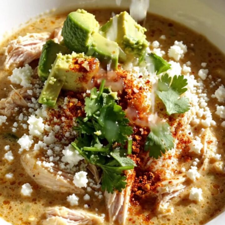A white stoneware Crockpot filled with creamy elote chicken stew topped with melted cheese and fresh cilantro.