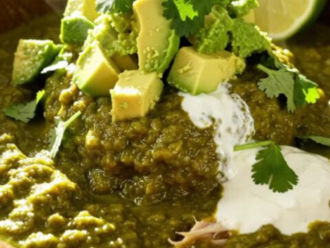 A close-up of a creamy tomatillo chicken and white bean bake in a white ceramic crockpot with bubbling melted cheese.