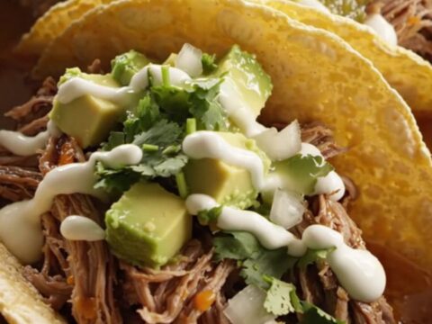 A cinematic shot of slow-cooked, shredded beef barbacoa topped with melted Oaxaca cheese in a stainless steel slow cooker.