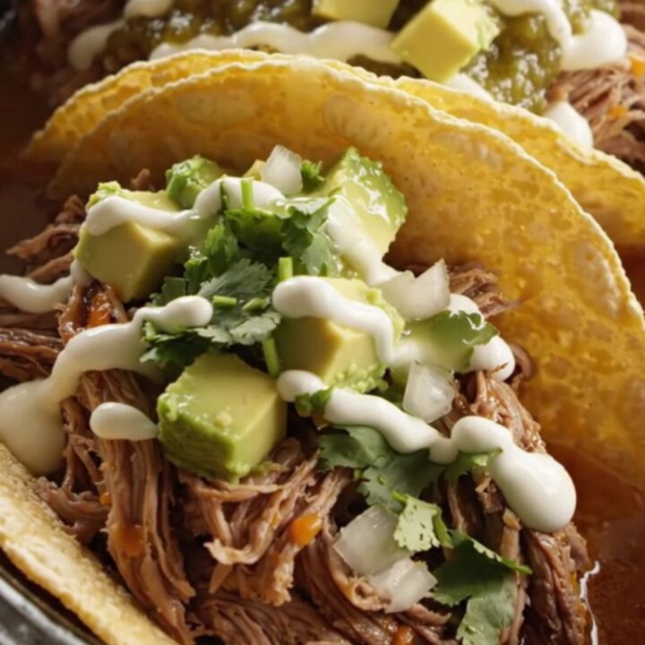A cinematic shot of slow-cooked, shredded beef barbacoa topped with melted Oaxaca cheese in a stainless steel slow cooker.
