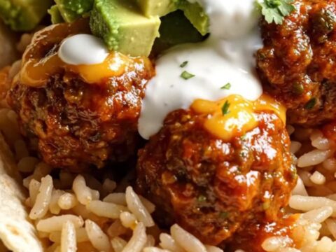 A glossy black slow cooker filled with juicy meatballs in red enchilada sauce and melted cheese.