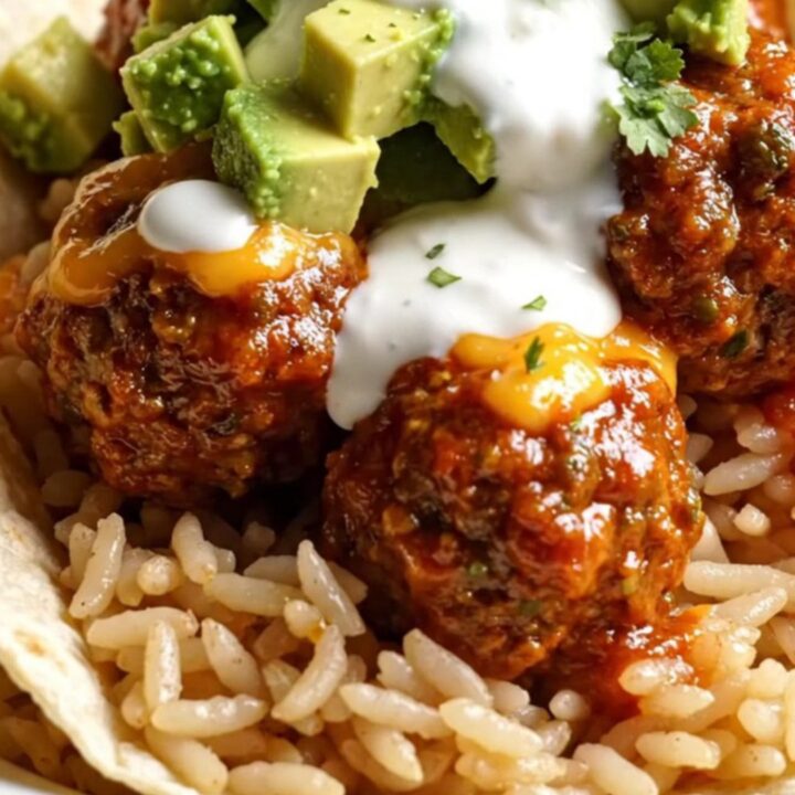 A glossy black slow cooker filled with juicy meatballs in red enchilada sauce and melted cheese.