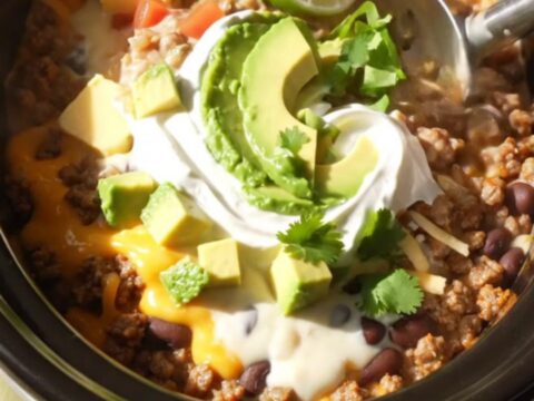 A ceramic slow cooker filled with a rich, cheesy Mexican beef and bean dip topped with fresh cilantro.