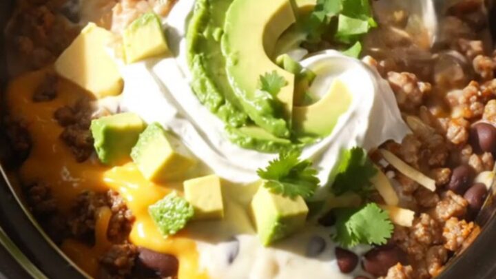 A ceramic slow cooker filled with a rich, cheesy Mexican beef and bean dip topped with fresh cilantro.
