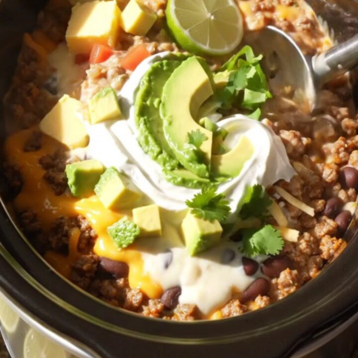 A ceramic slow cooker filled with a rich, cheesy Mexican beef and bean dip topped with fresh cilantro.