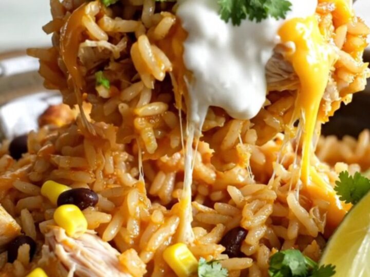 A steaming scoop of creamy chicken and rice casserole topped with melted cheese in a white stoneware slow cooker.