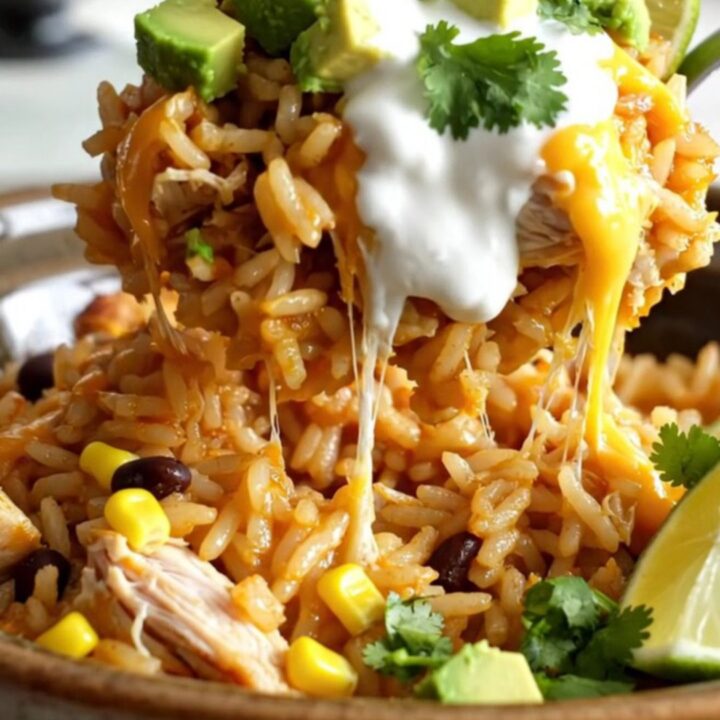 A steaming scoop of creamy chicken and rice casserole topped with melted cheese in a white stoneware slow cooker.