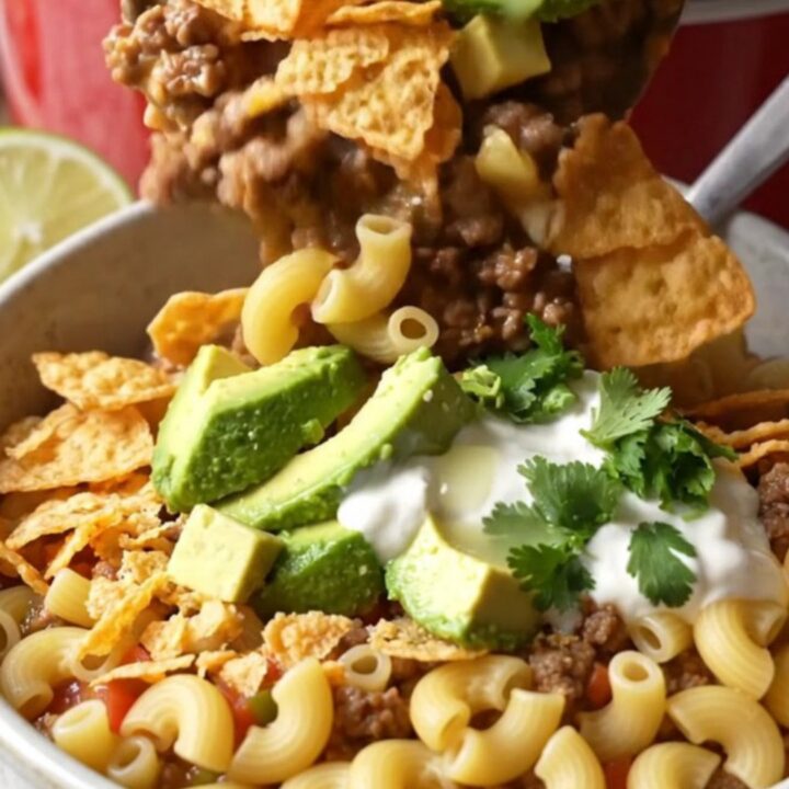 A glossy red slow cooker filled with creamy taco pasta bake topped with melted cheese and fresh cilantro.