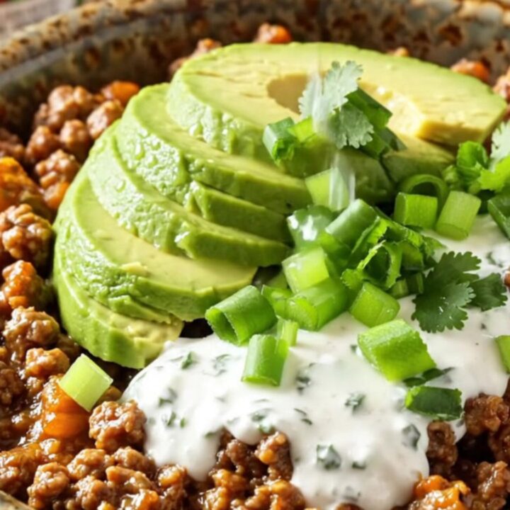 A close-up of the finished cheesy taco beef and potato hash in a matte black slow cooker.